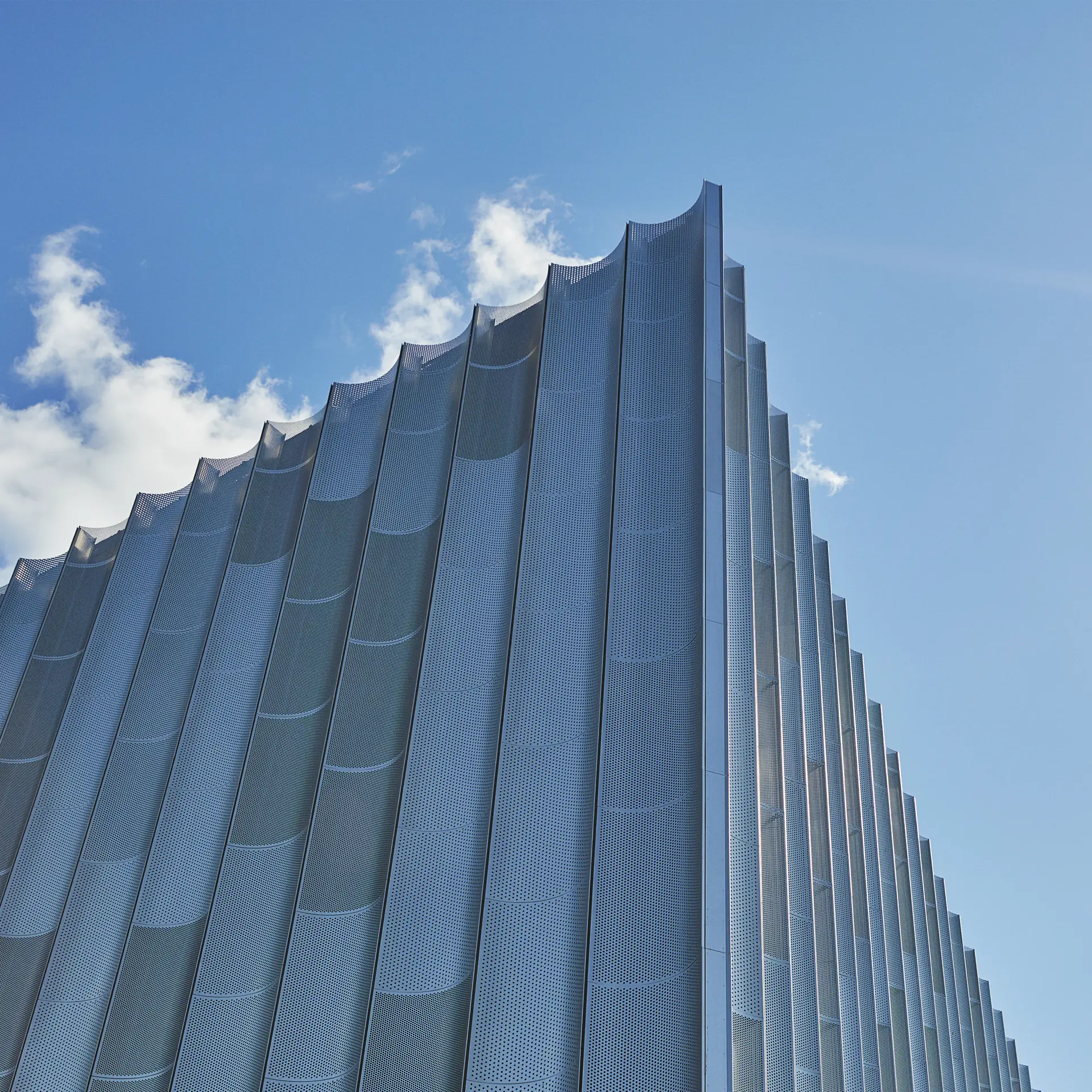 Arkitektonisk udsnit af facade på Bella Arena med blå himmel og sollys.