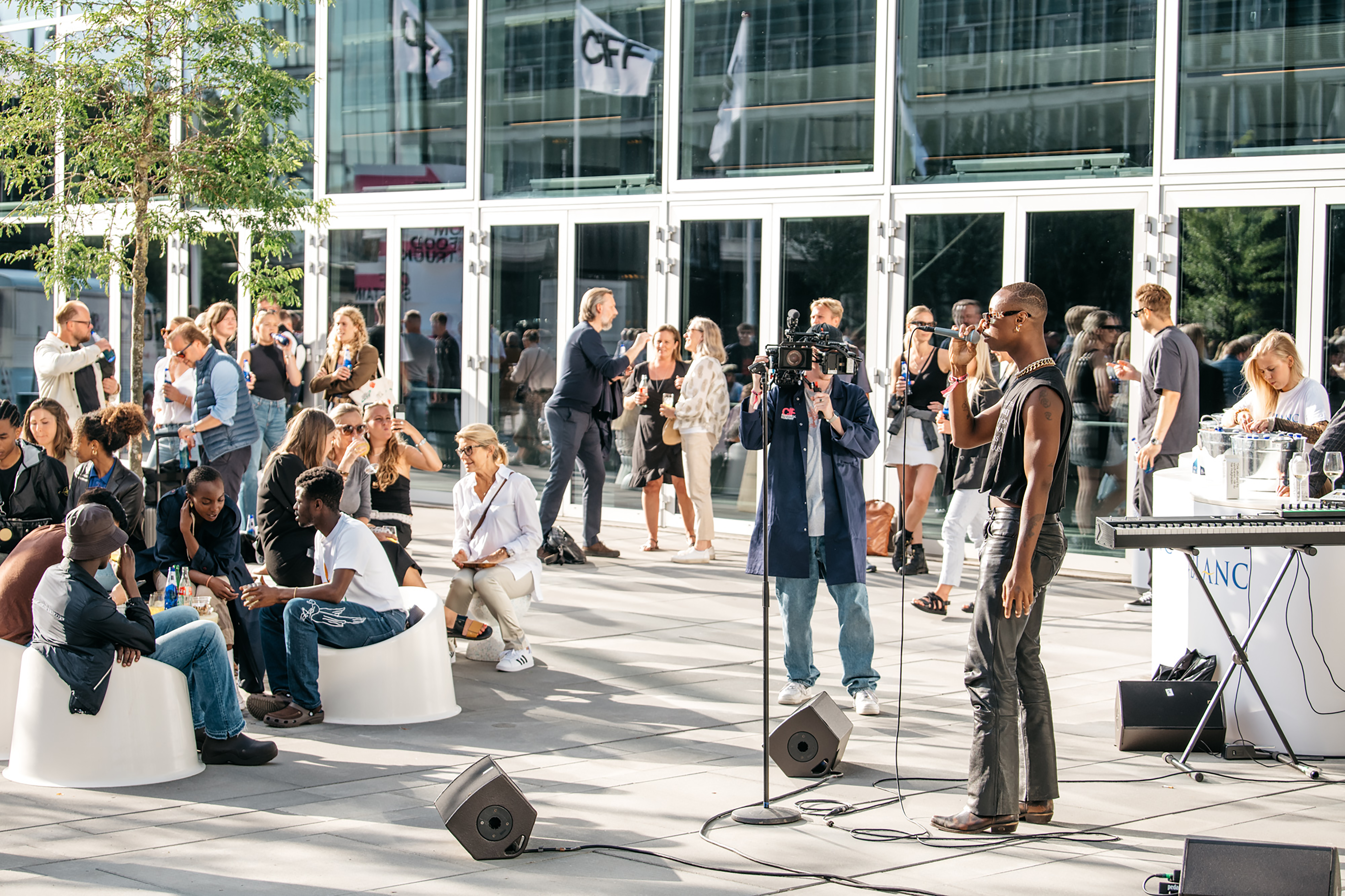 Mennesker samlet i udendørs loungeområde med intimkoncert foran Bella Center Copenhagen.
