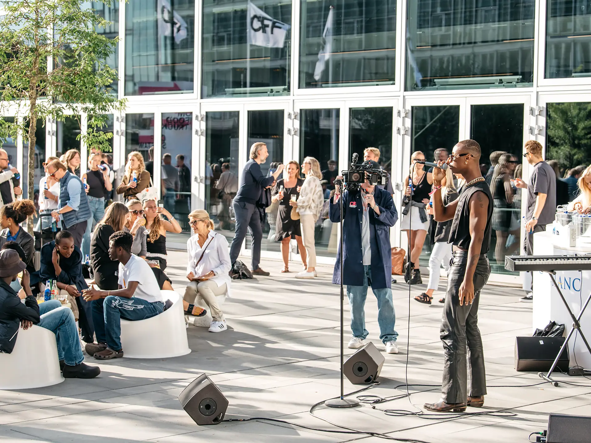 Mennesker samlet i udendørs loungeområde med intimkoncert foran Bella Center Copenhagen.