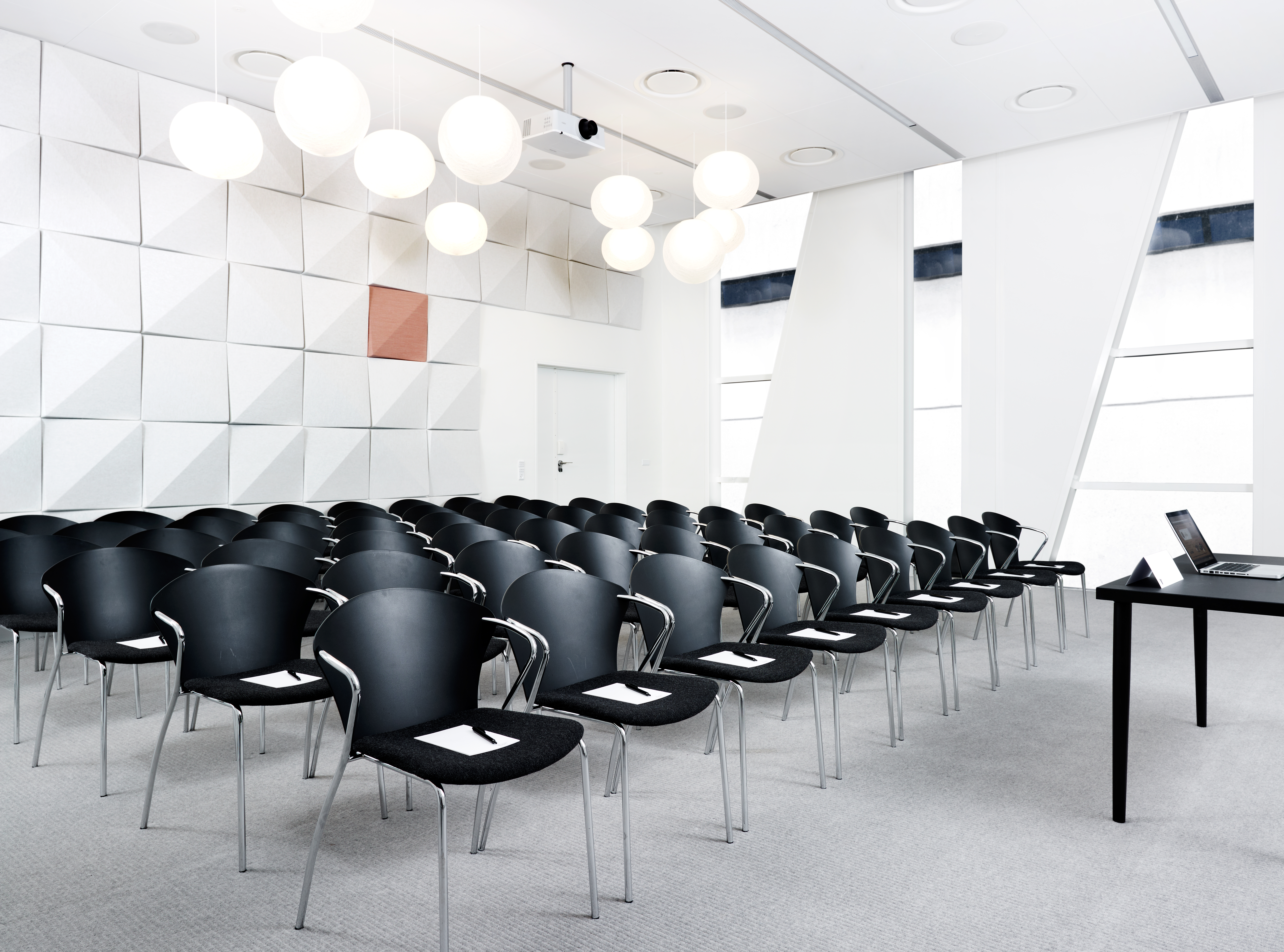 Lyst og moderne mødelokale i Bella Center med sorte stole og hvide vægge.