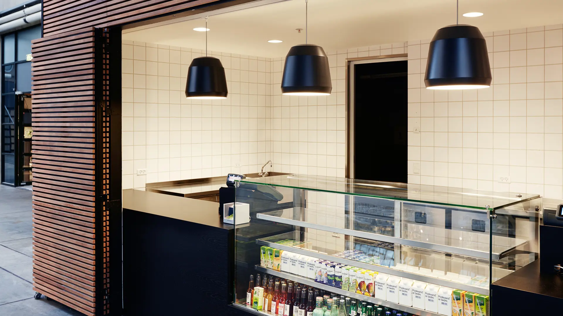 Food Grab i Hal E – moderne takeaway-disk med sort træbeklædning, hvide fliser og udstilling af kolde drikke og snacks.