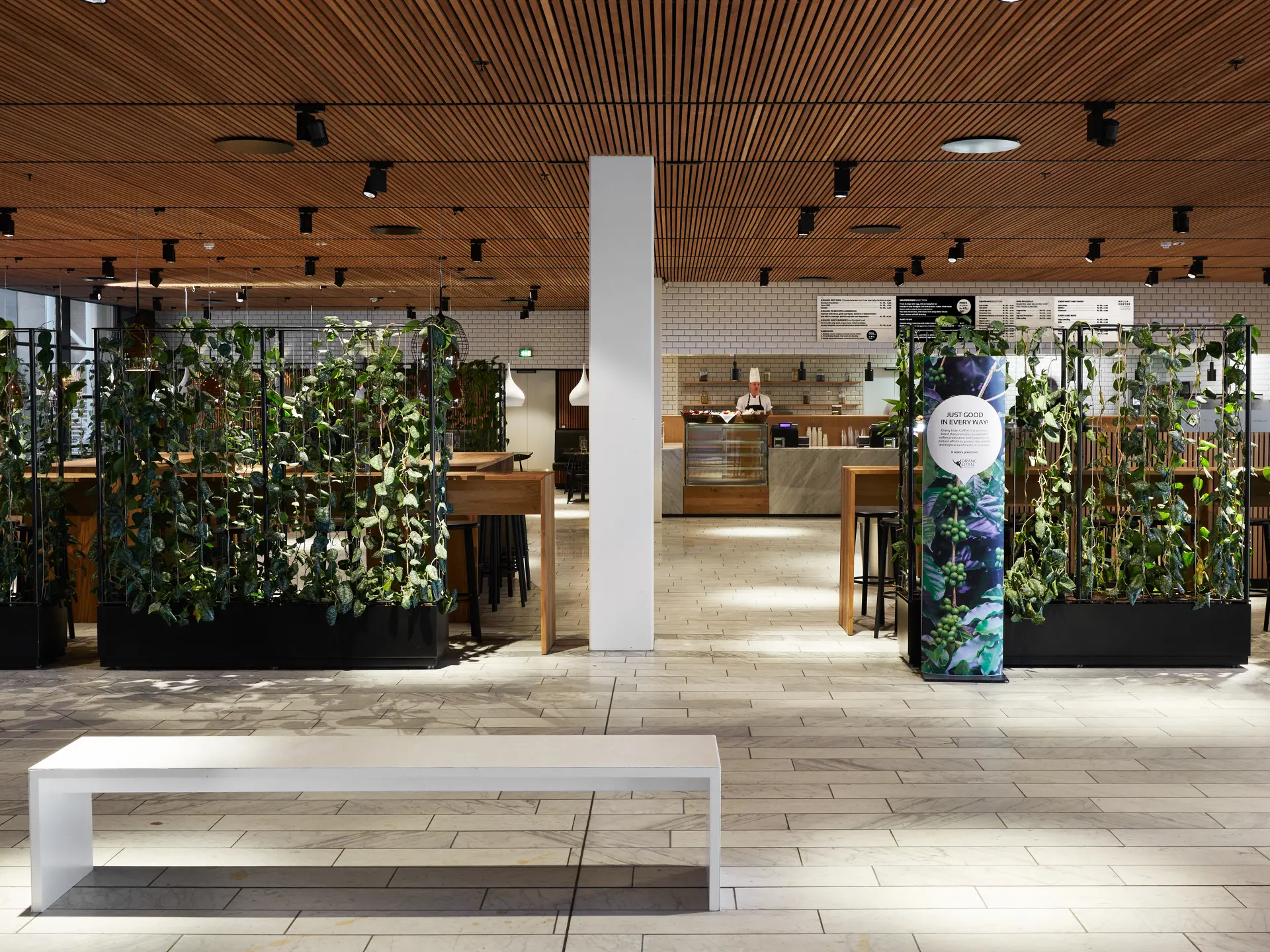The Gastro – indgangsområde med grøn plantevæg, hvide klinker og udsigt til caféområdet.