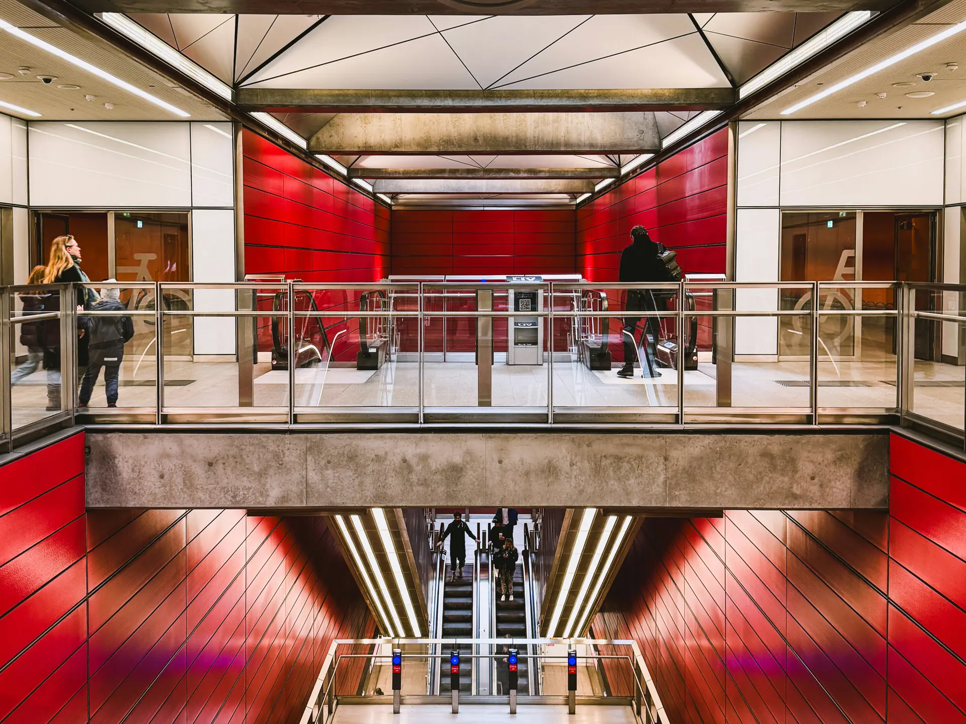 Rød metrostation i København med rulletrapper og passagerer