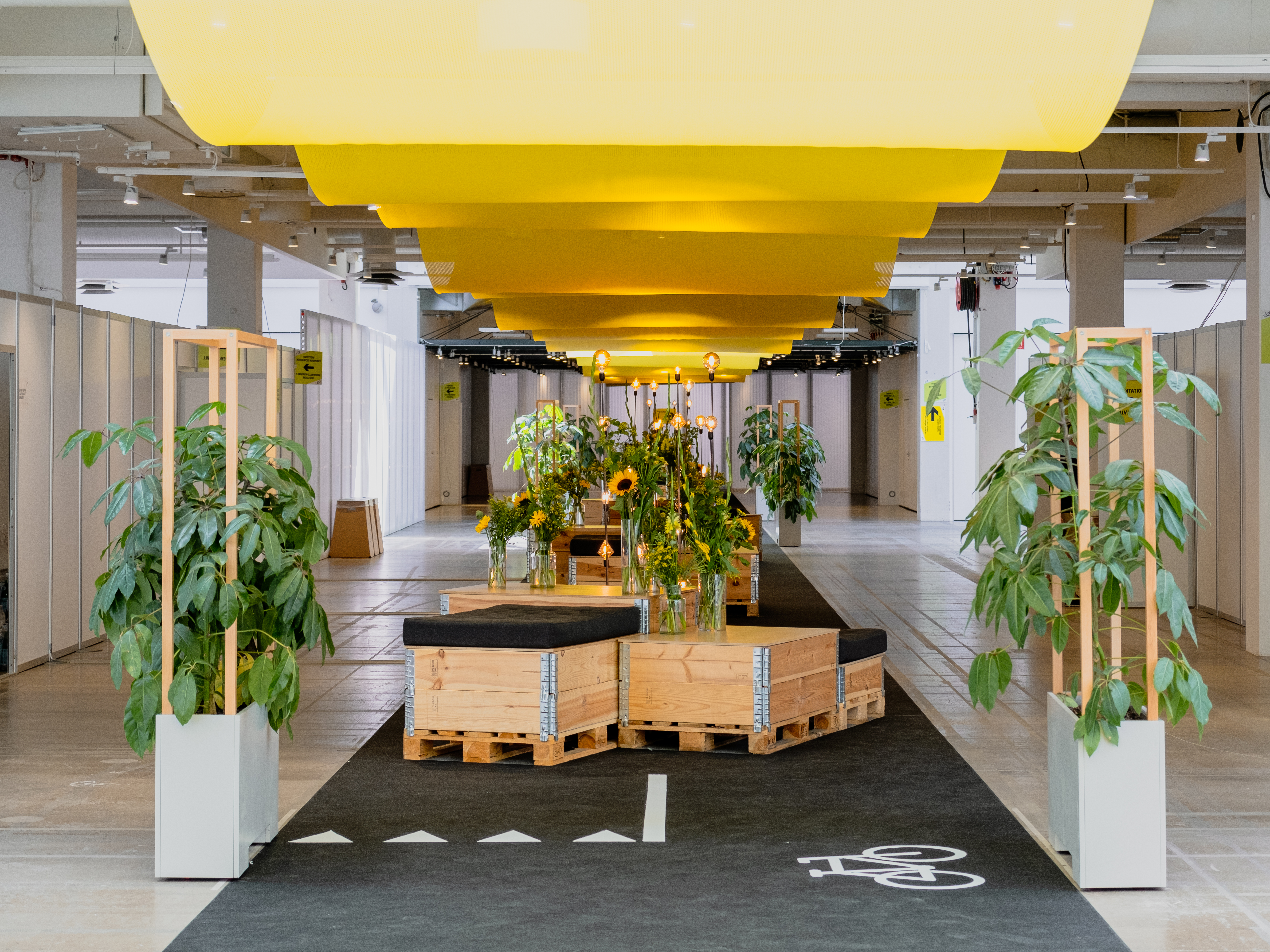 Moderne messedesign med planter, solsikker og gule gardiner i loftet.