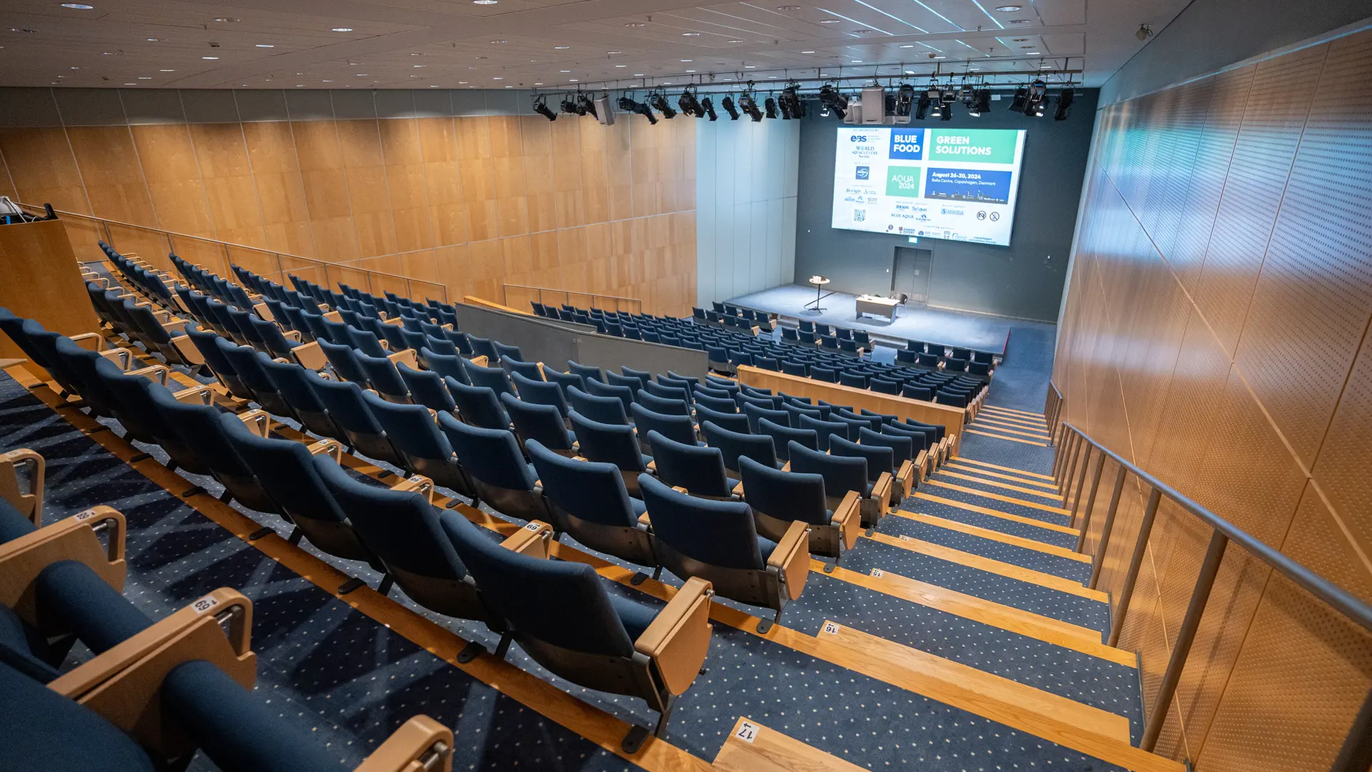 Auditorium 10-12 set fra bageste række med udsigt til scene og lærred under event i Bella Center, København.