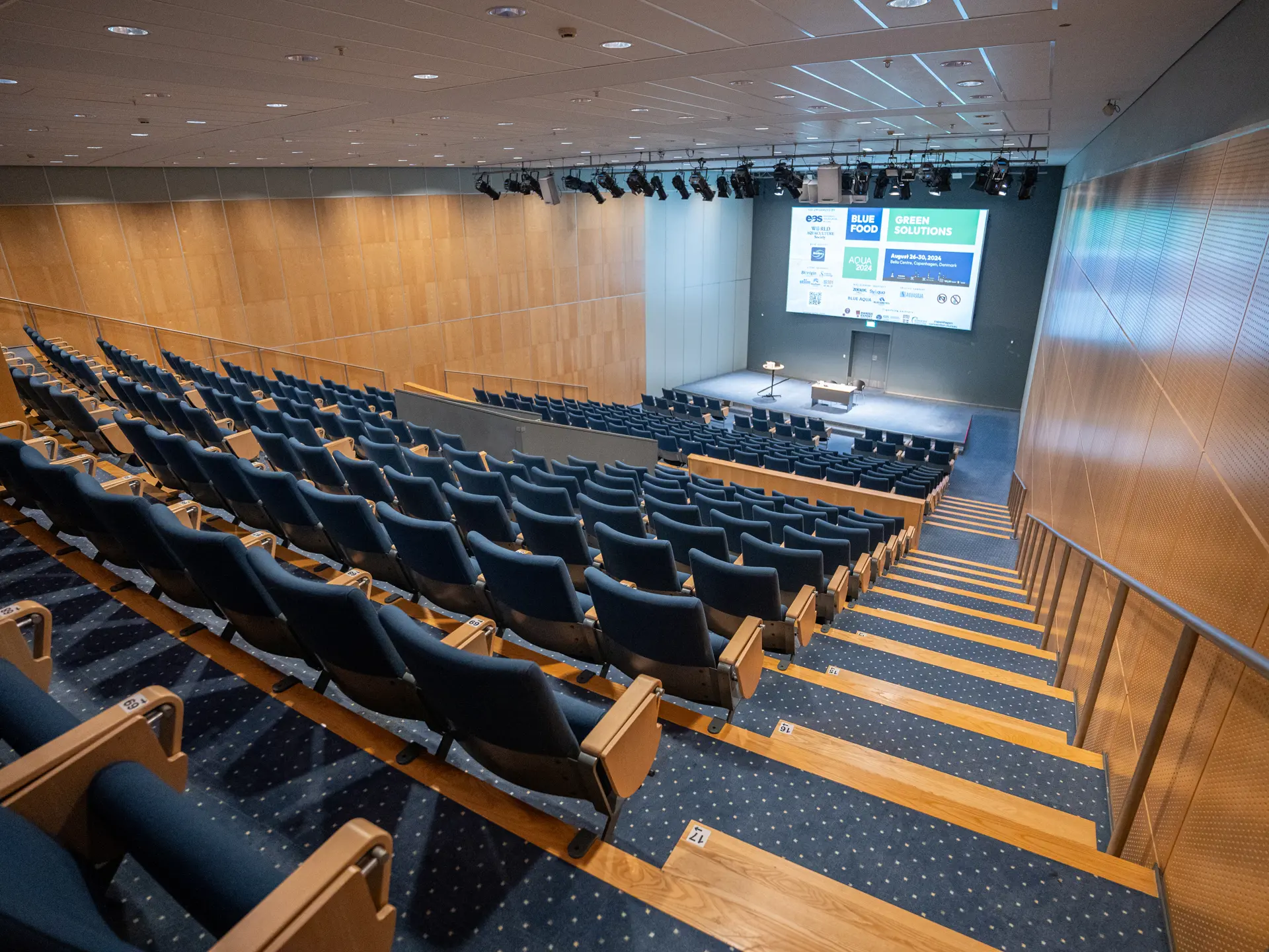 Auditorium 10-12 set fra bageste række med udsigt til scene og lærred under event i Bella Center, København.