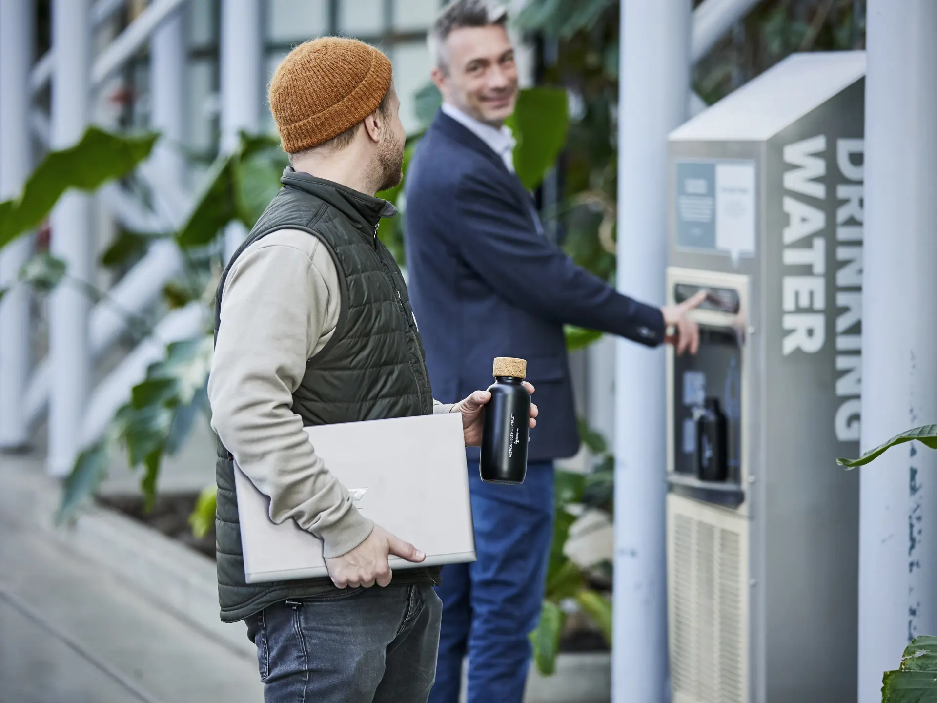 To smilende medarbejdere i Bella Center, der taler sammen ved en vandautomat.