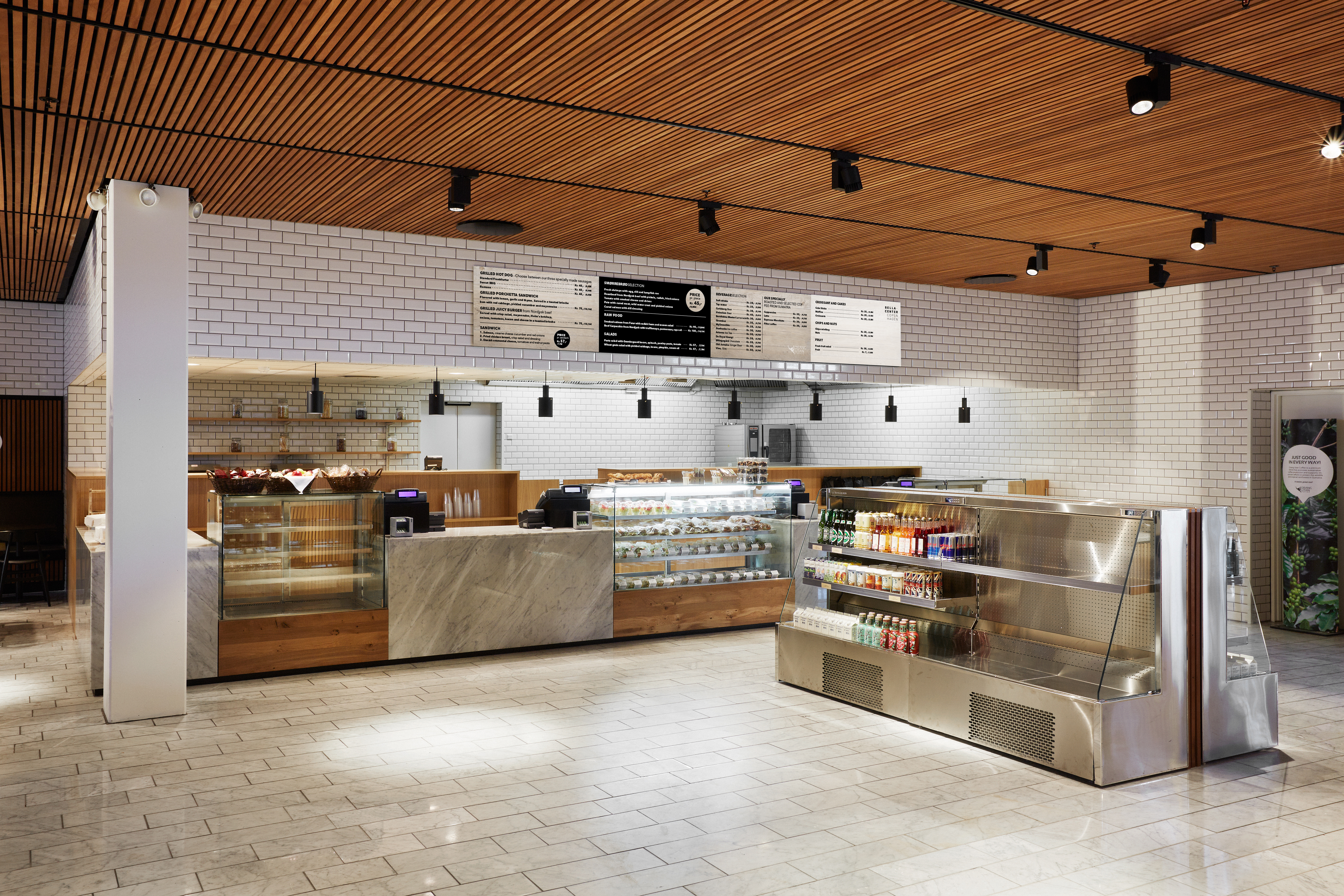 The Gastro – lyst og rummeligt caféområde med træloft, hvide fliser og lange diske med mad og drikke.