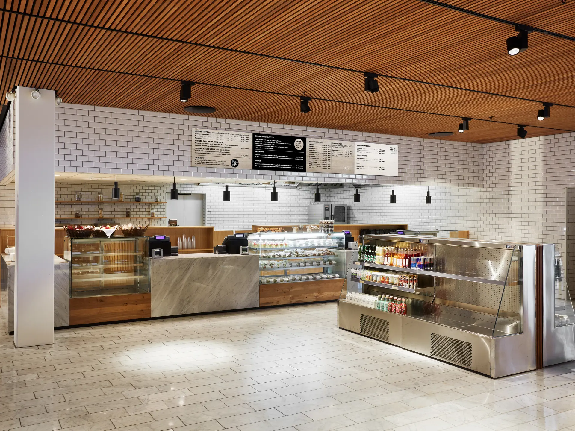 The Gastro – lyst og rummeligt caféområde med træloft, hvide fliser og lange diske med mad og drikke.