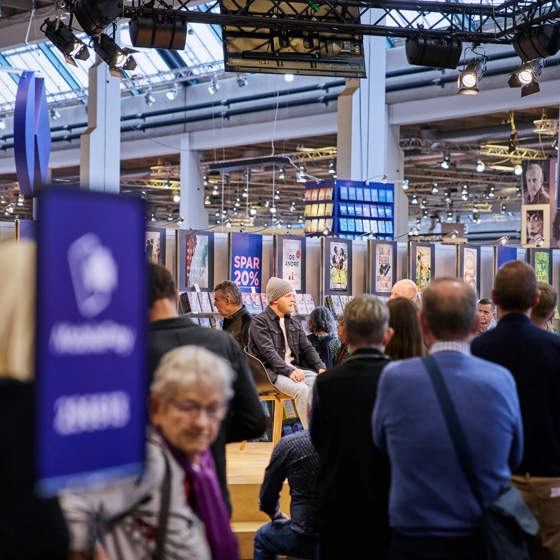 Publikum til oplæg på Bogforum messe i Bella Center omgivet af stande og bannere.