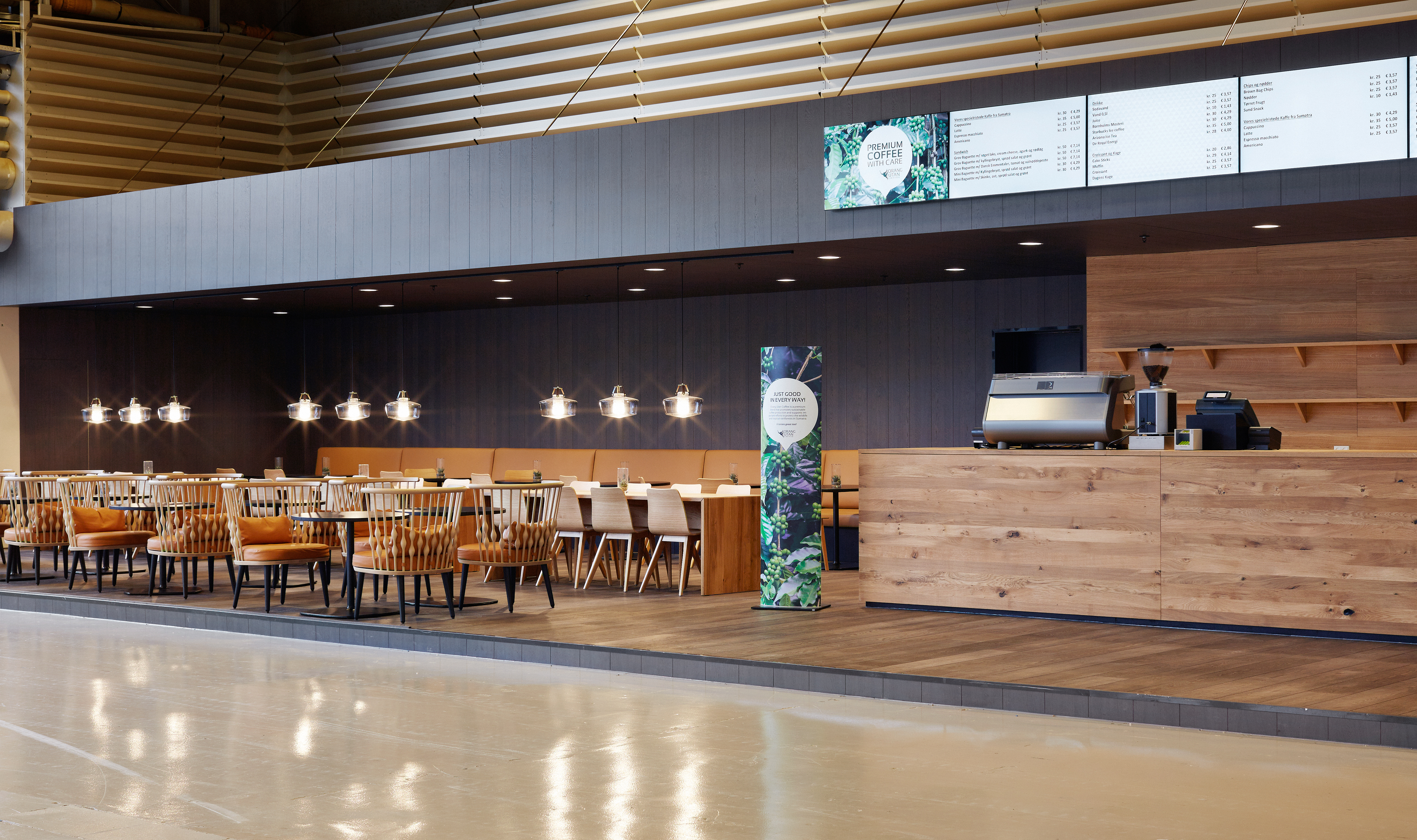 Orangu Lounge – tomt caféområde med lyse træmøbler, varme farver og hyggelig belysning.