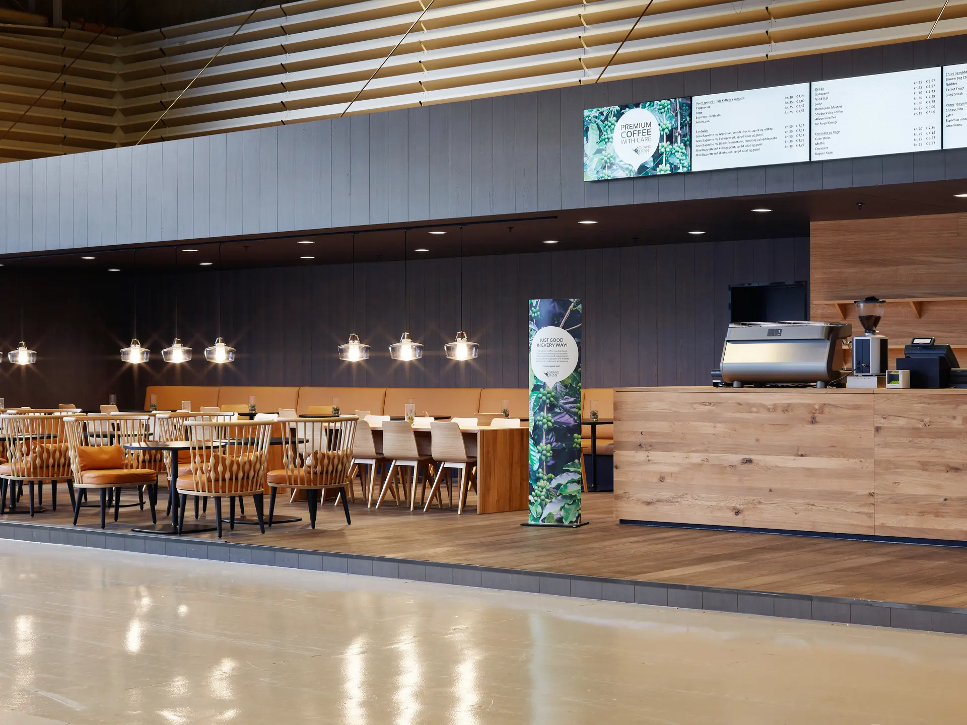 Orangu Lounge – tomt caféområde med lyse træmøbler, varme farver og hyggelig belysning.